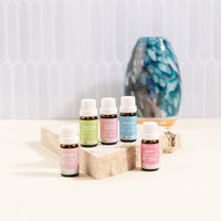 Set of essential oil bottles on a wooden block with a decorative vase in the background.
