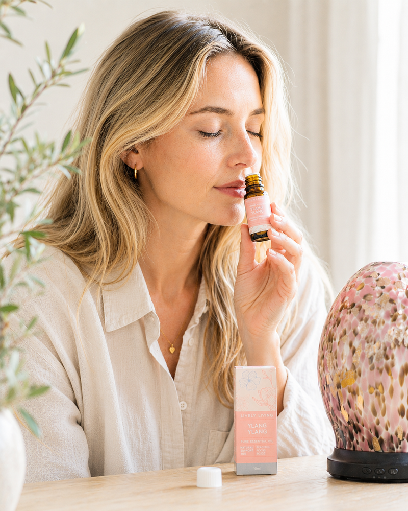 Woman smelling a pink bottle of perfume with a decorative lamp and plant in the background