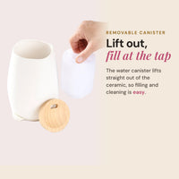 Hand lifting the water canister out of a white ceramic Aroma-Fern diffuser with its bamboo lid set aside, headline Lift out, fill at the tap