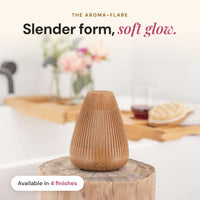 Wood-look Aroma-Flare Diffuser with slatted fins on a timber stump beside a bath tray, headline Slender form, soft glow, available in 4 finishes