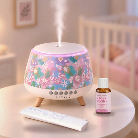 Aroma-Snooze Plus with a floral cover releasing mist on a nursery table beside its remote and Aroma Snooze certified organic oil