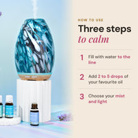 Aroma-Swish peacock glass diffuser on a white pedestal beside Lively Living oils, with three steps: fill with water to the line, add 2 to 5 drops of oil, and choose your mist and light