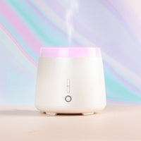 Five aroma diffusers in various colors including white, black, rose gold, and wood finish, displayed side by side.