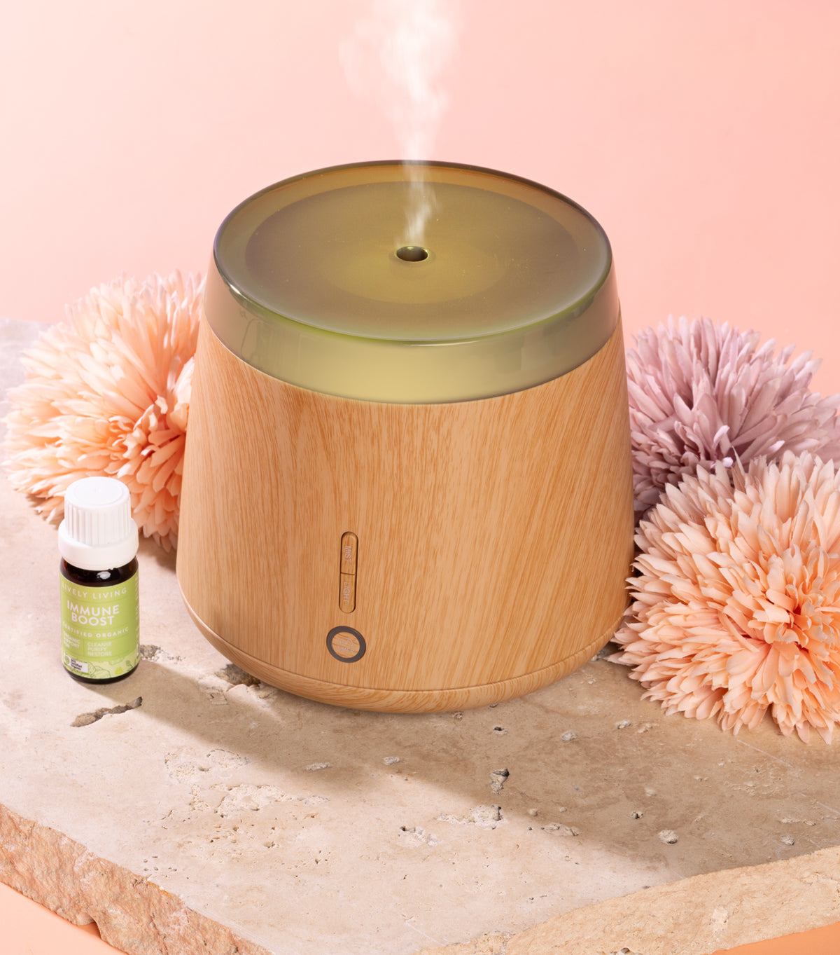 Wooden diffuser with steam, bottle, and decorative flowers on a light pink background