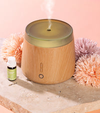 Wooden diffuser with steam, bottle, and decorative flowers on a light pink background
