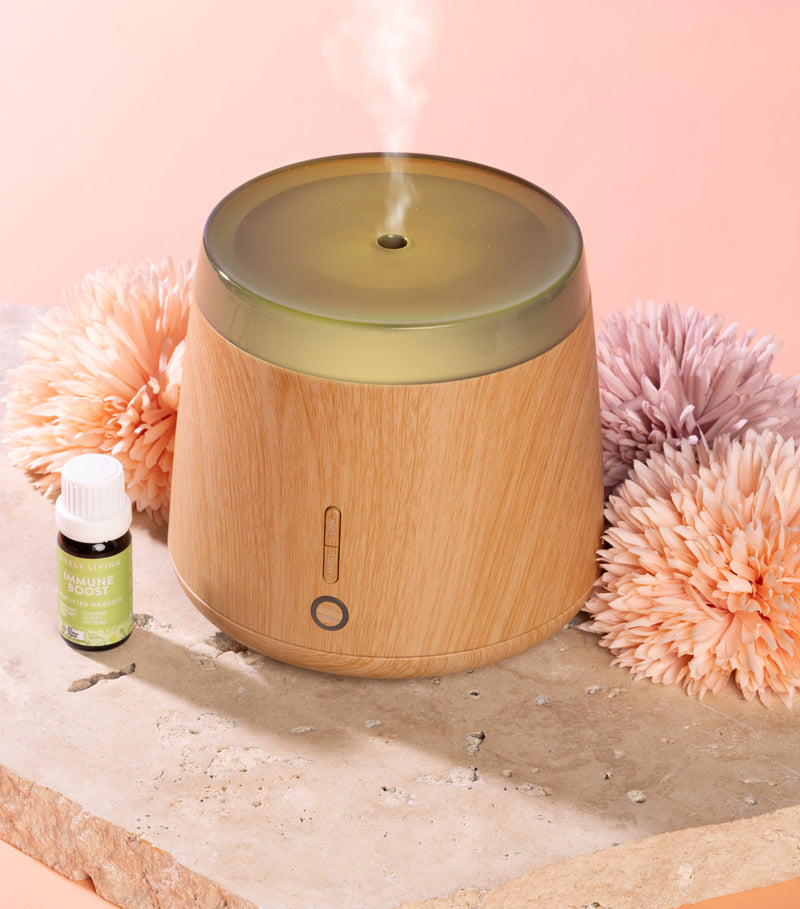 Wooden diffuser with steam, bottle, and decorative flowers on a light pink background