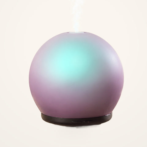 Lively Living Aroma-Halo glass diffuser with an iridescent mauve finish, aqua glow and black base, releasing mist on a cream background