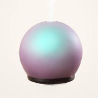 Lively Living Aroma-Halo glass diffuser with an iridescent mauve finish, aqua glow and black base, releasing mist on a cream background
