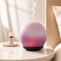 Purple diffuser emitting steam on a marble surface with a bottle of essential oil in the background.