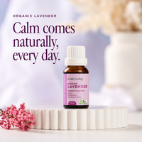 Lively Living Organic Lavender 15ml bottle on a white fluted pedestal with sprigs of pink wax flower, against a soft lilac background with Organic Lavender headline text