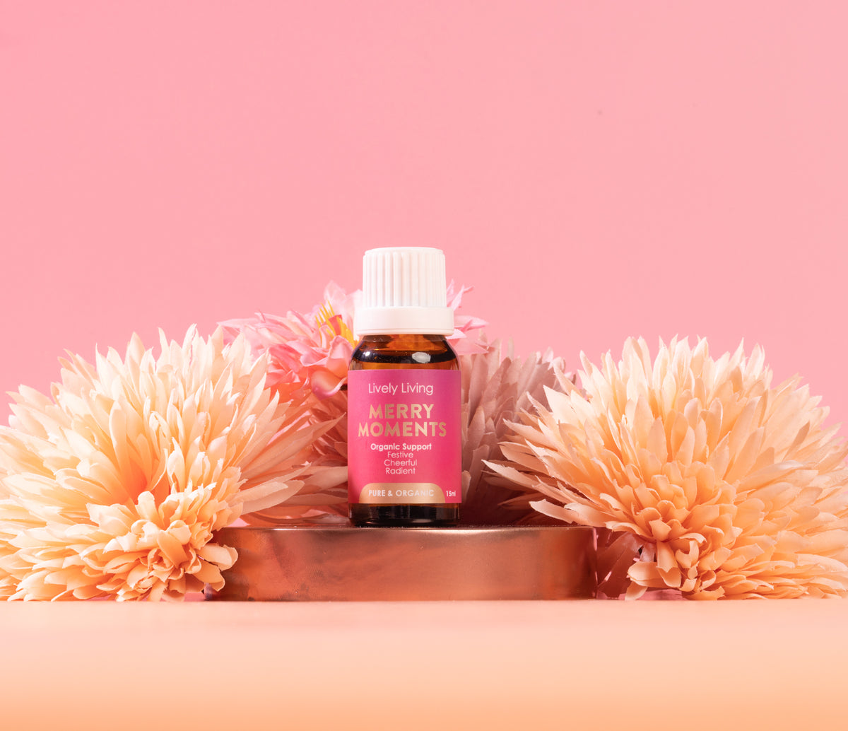 Bottle of 'Every Moment' essential oil with flowers on a pink background