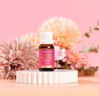 Bottle of Lively Living Merry Moments essential oil on a white stand with pink flowers in the background