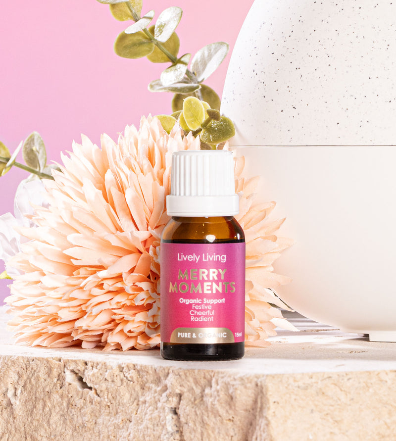 Bottle of Lively Living 'Merry Moments' product with decorative flowers and a pink background