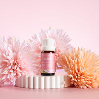 Lively Living Certified Organic Sleep Essential Oil Blend. Sitting on a rippled white plinth surrounded by pink and orange flowers. 