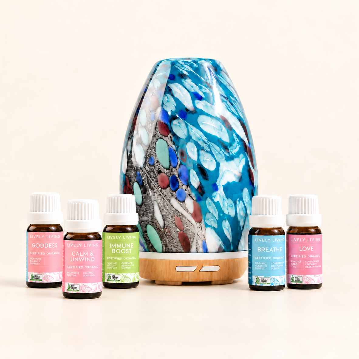 Aroma-Swish Diffuser in hand-shaped blue, teal and white peacock glass on a wood-look base, with five Lively Living certified organic oils from the Daily Balance Collection