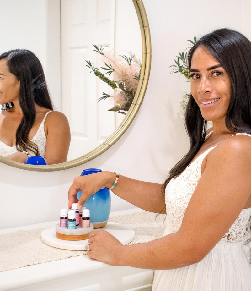 Woman in a white dress sitting at a vanity table with a round mirror and decorative items.