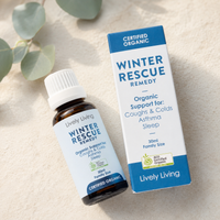 A small amber bottle and matching box of Lively Living Winter Rescue Remedy, photographed on a light beige textured surface with soft green leaves in the background.