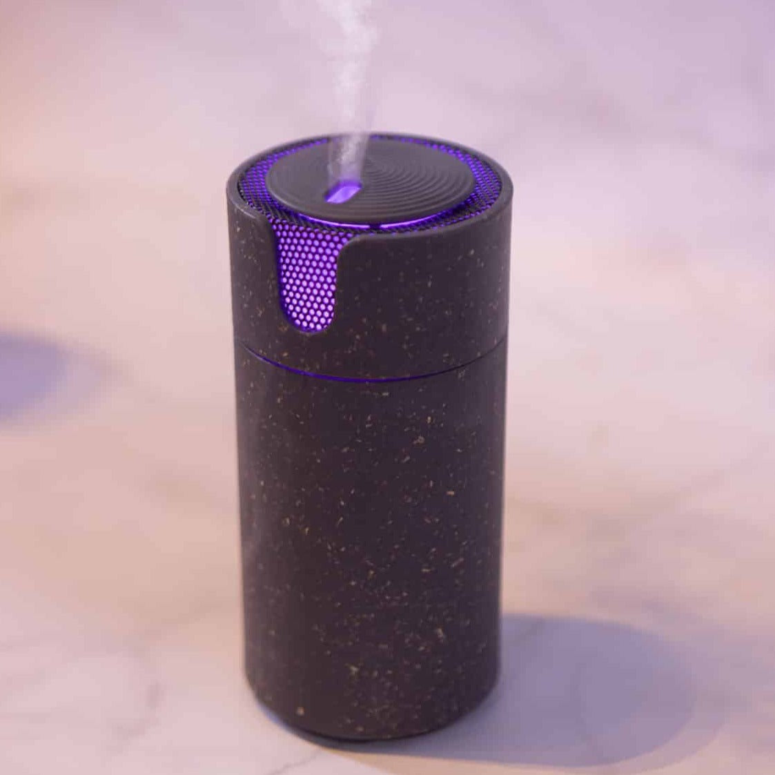 Charcoal speckled Aroma-Recharge cordless diffuser glowing purple and releasing mist