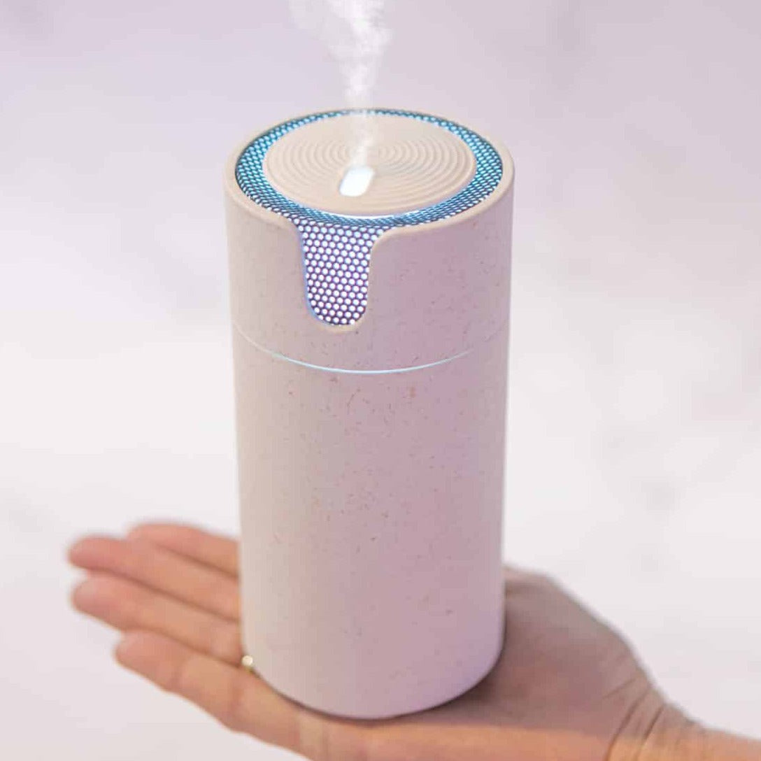Hand holding the stone speckled Aroma-Recharge cordless diffuser glowing blue as it releases mist