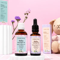 Baby Massage Oil and Baby Tummy Oil with boxes on white pedestals beside a plush bunny and purple flowers