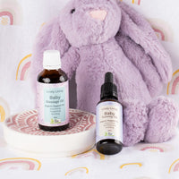 Lively Living Baby Massage Oil and Baby Tummy Oil on a pink dish in front of a lilac plush bunny